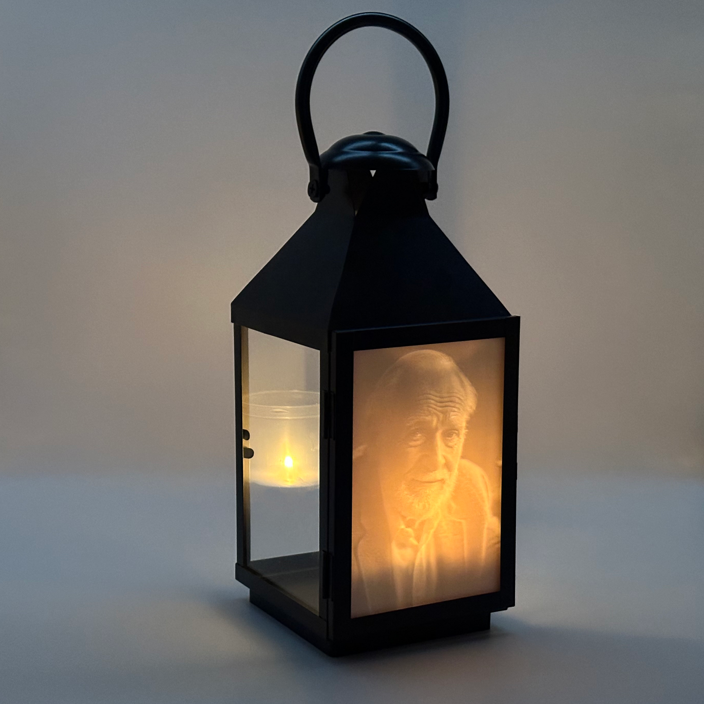 En svart gravlykta som lyser upp ett 3D-utskrivet porträtt (litofan) med ett ljus.